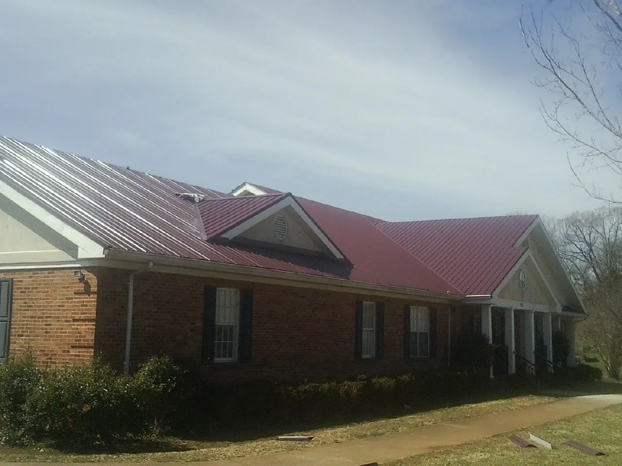 Red metal roof with gabled entries on a long brick building, from a Hail Damage Roof Repair job in Walterville