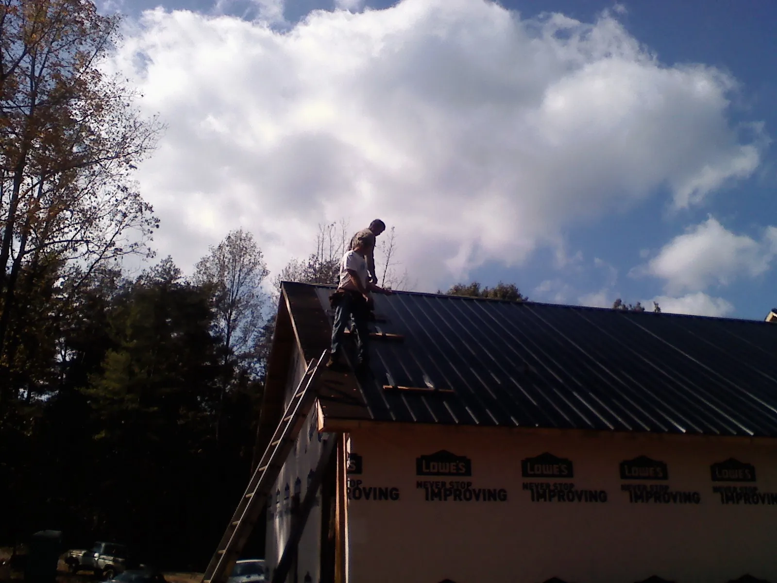 Roofer fastening dark metal panels high against a cloudy sky, from a Roof Inspection job in Walterville
