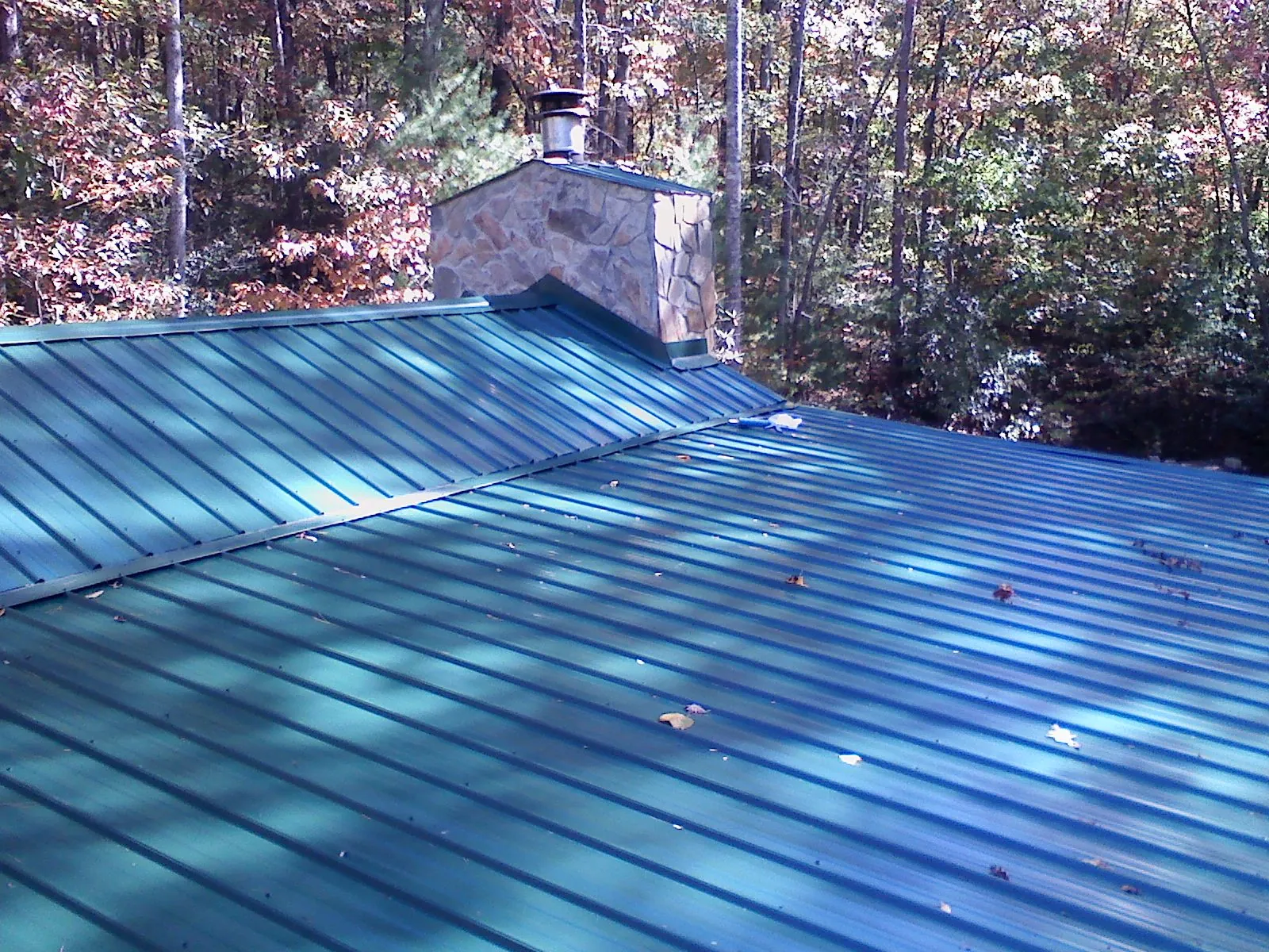 New green metal roof and stone chimney surrounded by autumn woods in Walterville