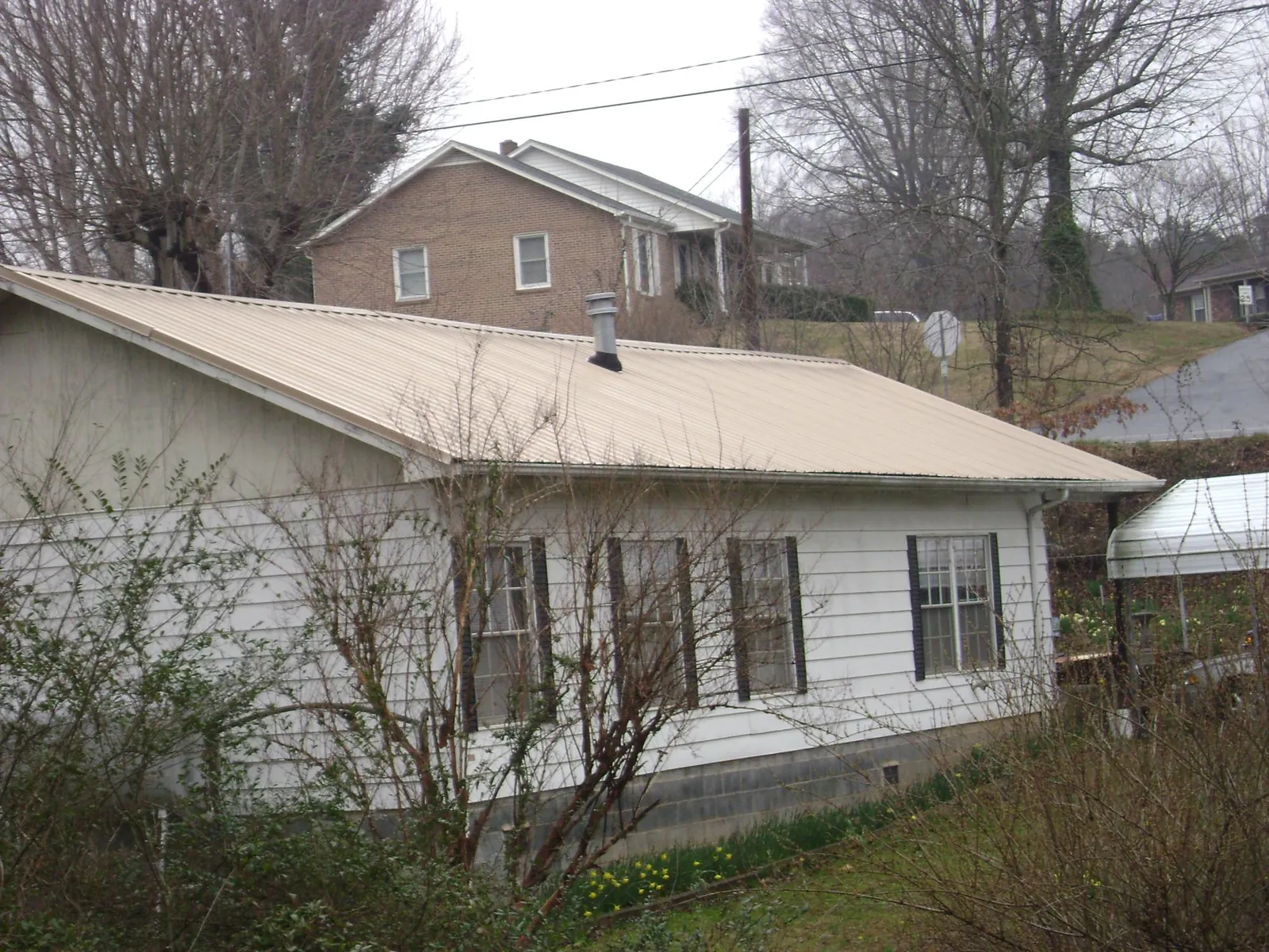 Tan metal roof on a white sided house set into a hillside — Commercial Roofing by Roofing Brothers in Walterville
