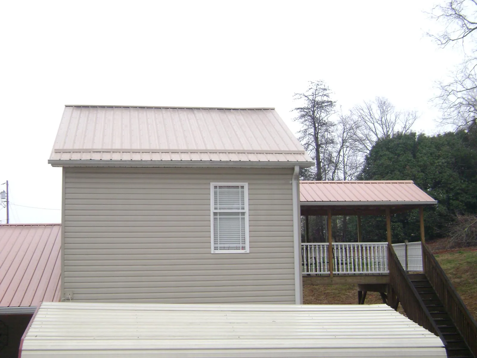 Tan metal roofs on a two story addition and attached porch, from a Roof Replacement job in Walterville